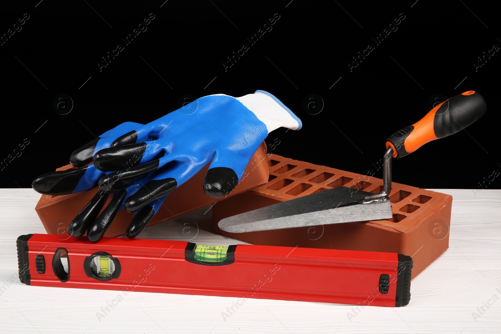 Photo of Red bricks, building level, gloves and trowel on white wooden table. Construction tools