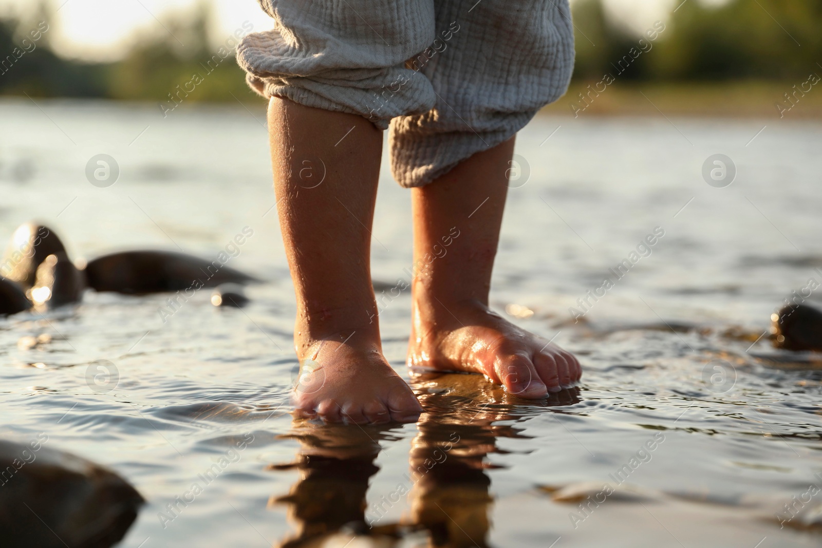 Photo of Cute little girl standing in water outdoors, closeup. Child enjoying beautiful nature