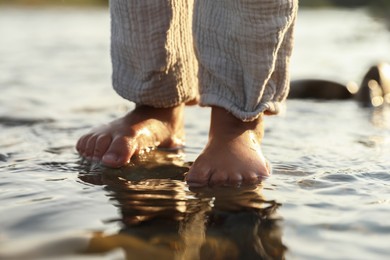 Photo of Cute little girl standing in water outdoors, closeup. Child enjoying beautiful nature