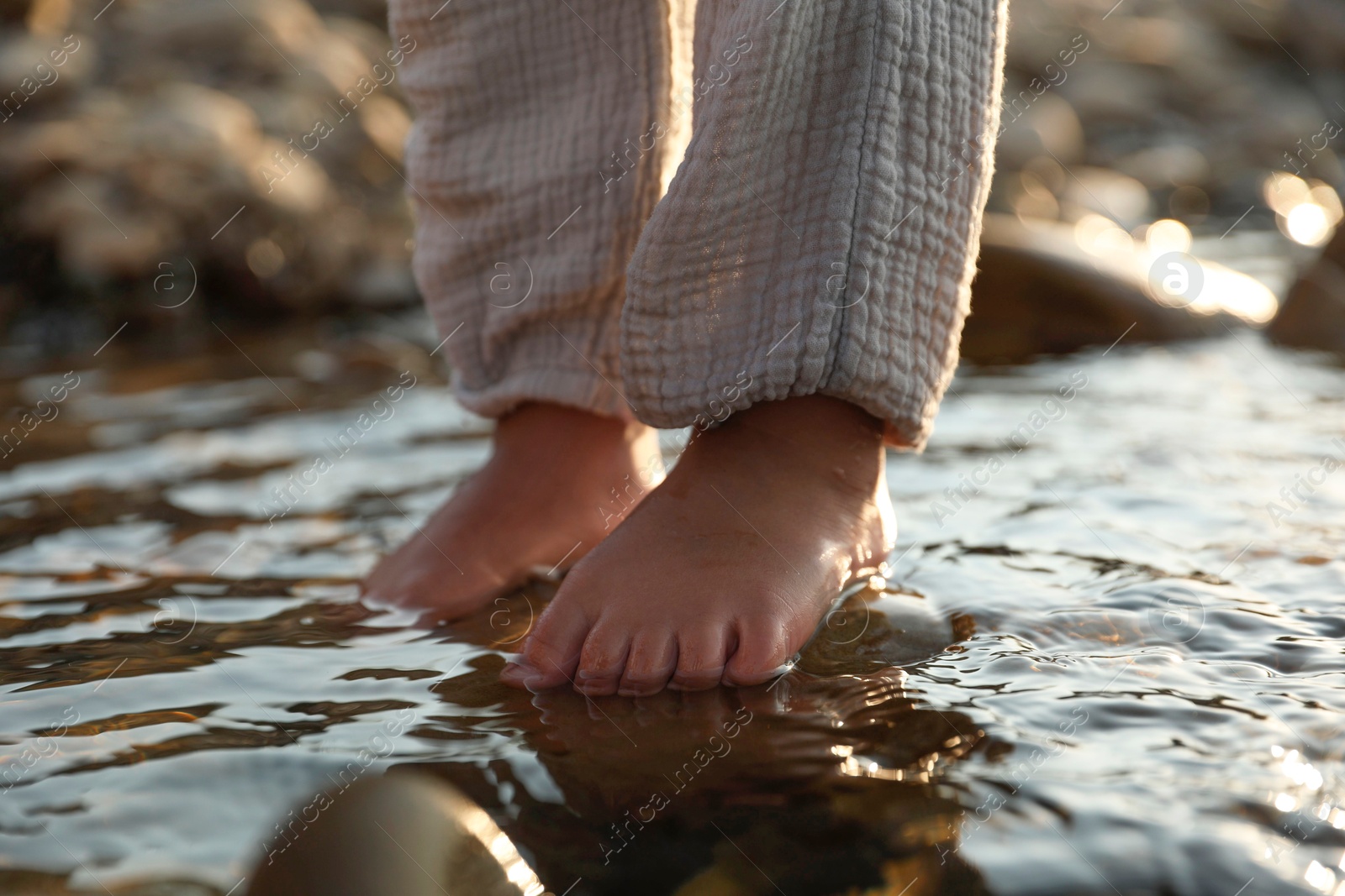 Photo of Cute little girl standing in water outdoors, closeup. Child enjoying beautiful nature