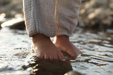 Photo of Cute little girl standing in water outdoors, closeup. Child enjoying beautiful nature