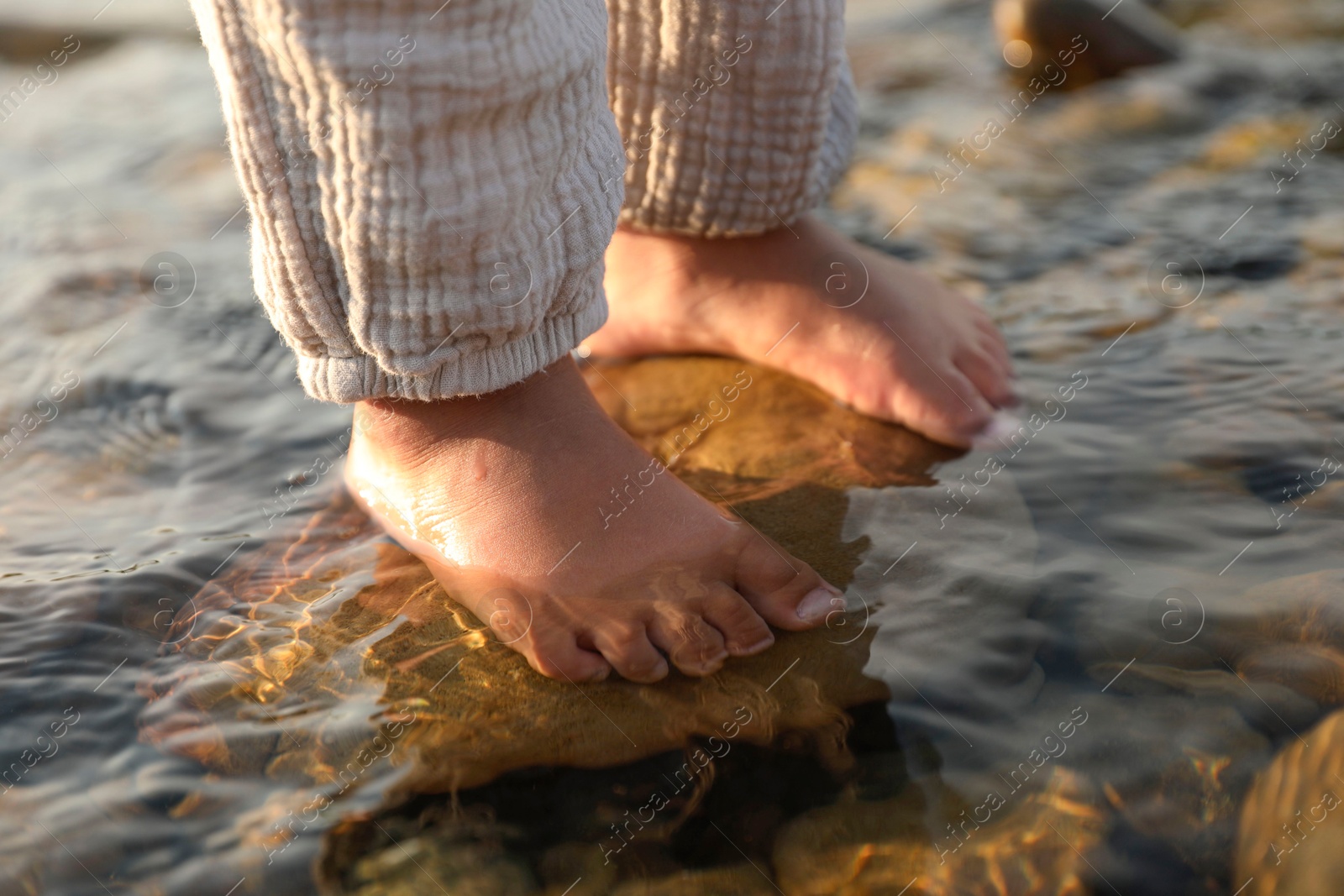 Photo of Cute little girl standing in water outdoors, closeup. Child enjoying beautiful nature