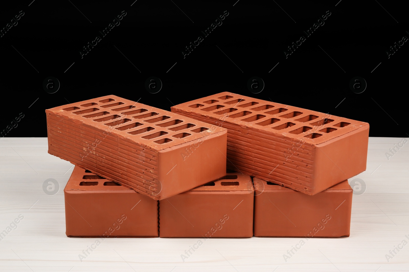 Photo of Many red bricks on light wooden table against black background. Building material