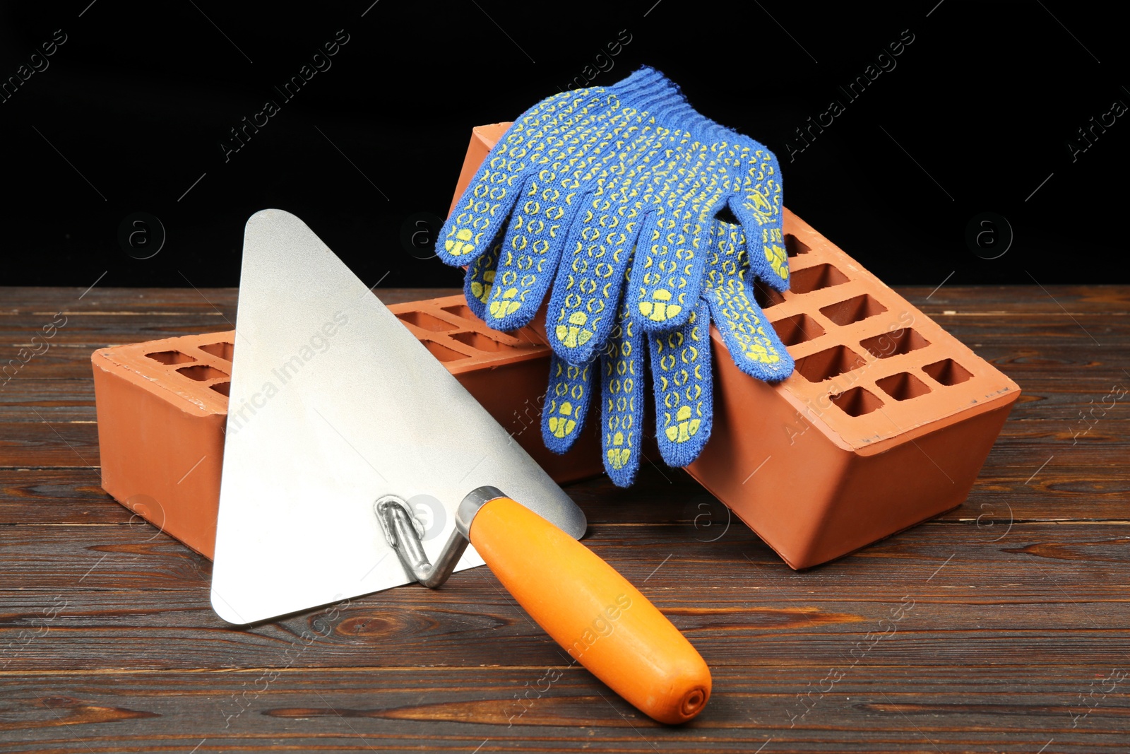 Photo of Red bricks, putty knife and rubber gloves on wooden table. Building material