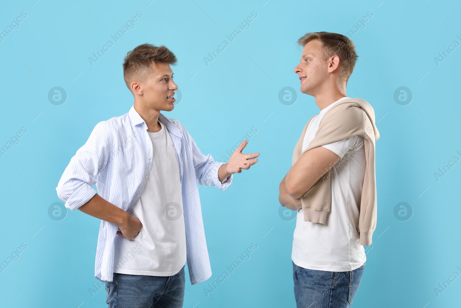 Photo of Two young brothers talking on light blue background