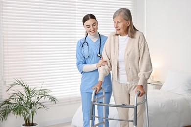 Photo of Nurse helping senior woman with walking frame in clinic