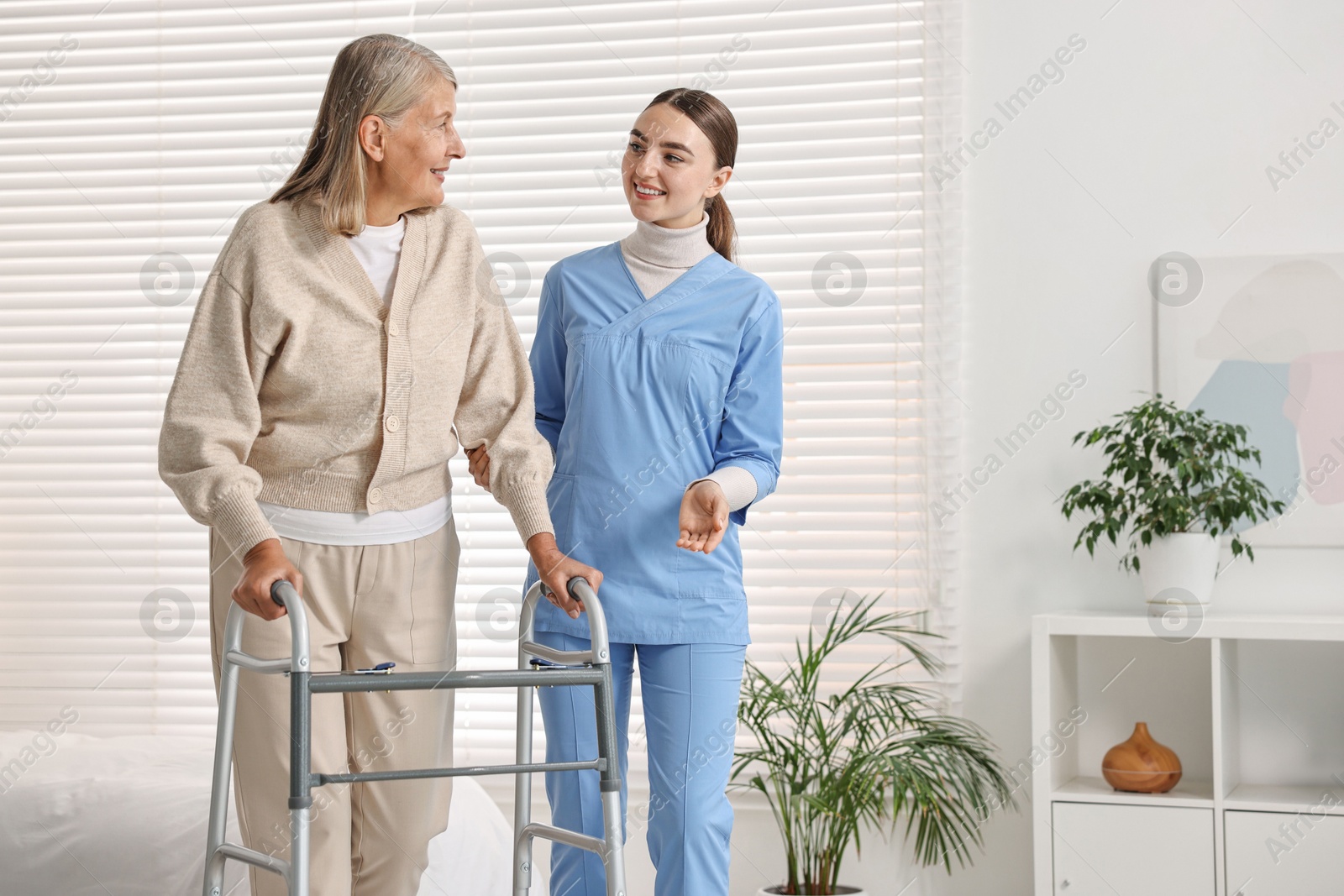 Photo of Nurse helping senior woman with walking frame in clinic