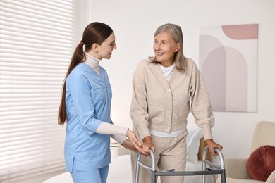 Nurse helping senior woman with walking frame in clinic