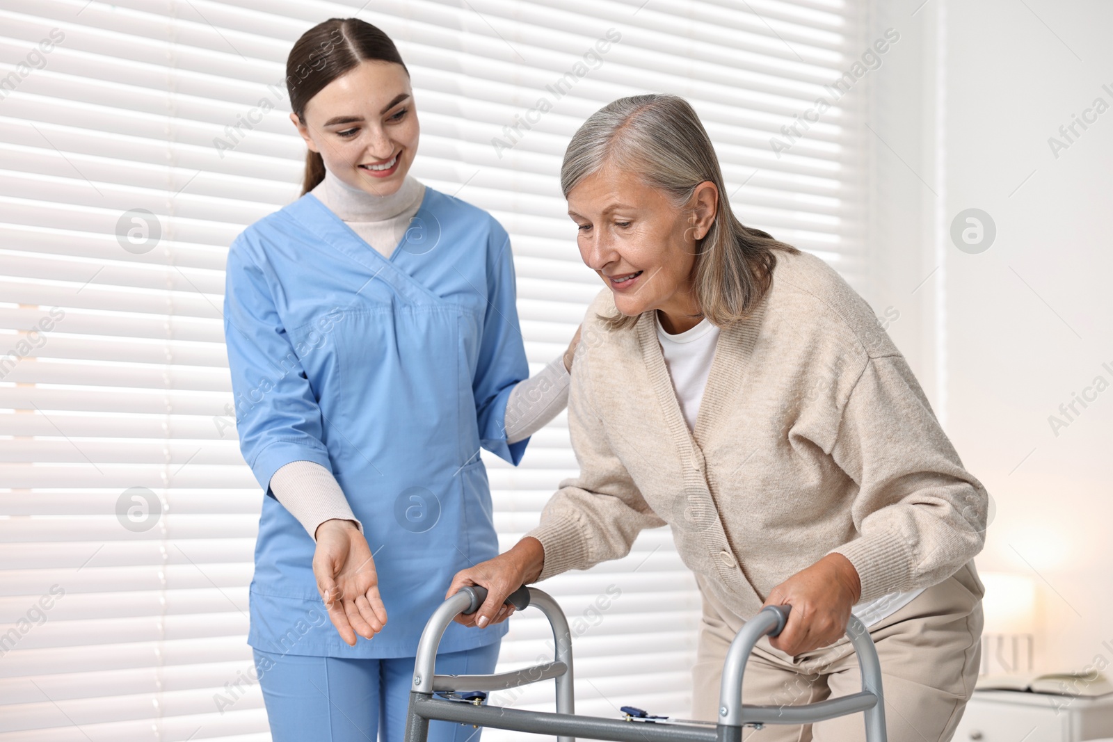 Photo of Nurse helping senior woman with walking frame in clinic