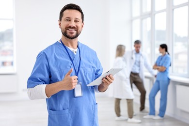 Healthcare workers in hospital, selective focus. Nurse with tablet showing thumbs up indoors