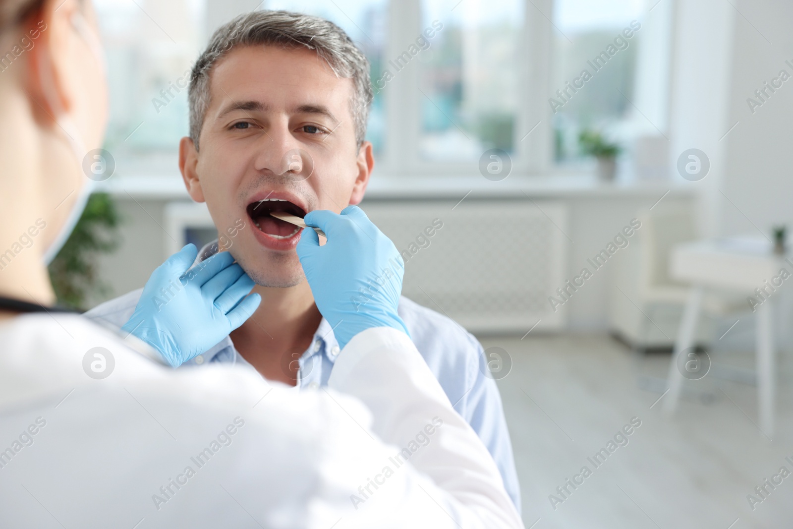 Photo of Doctor examining man's throat with tongue depressor in clinic