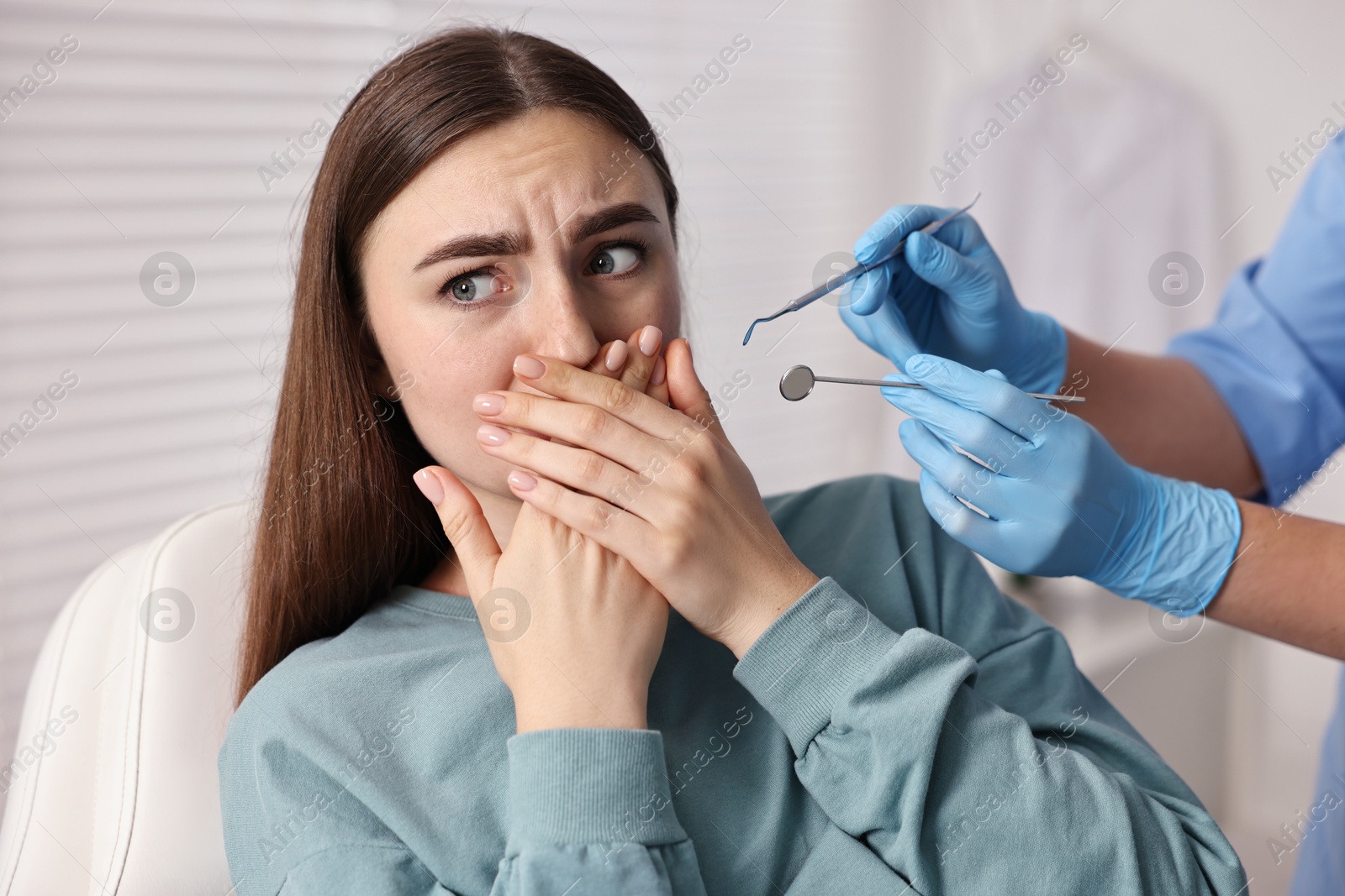 Photo of Dental phobia. Dentist working with scared woman in clinic, closeup