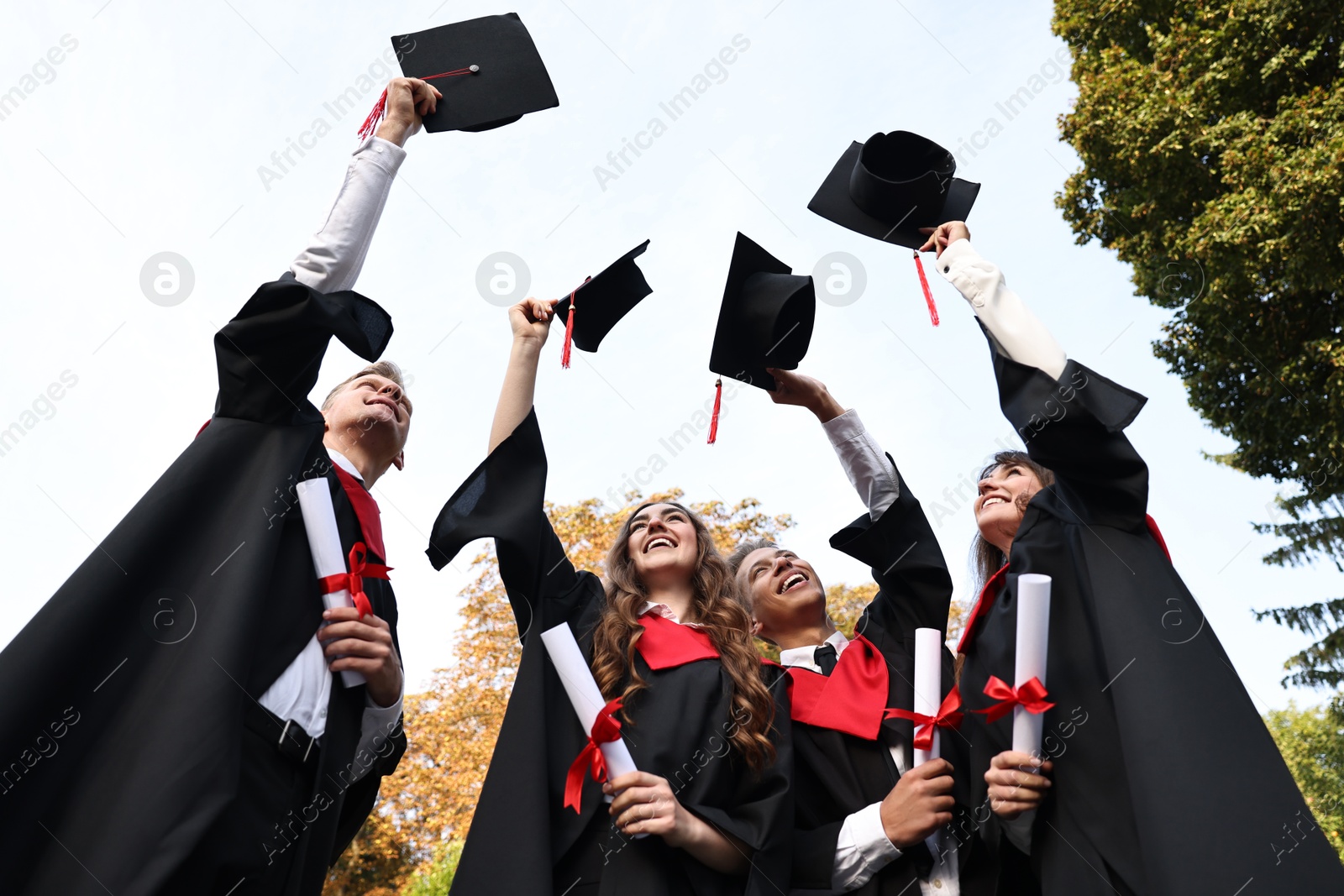 Photo of Graduation ceremony. Group of students with diplomas throwing hats outdoors, low angle view