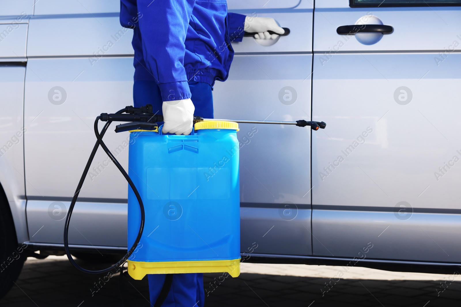 Photo of Pest control worker with spray tank near gray minibus outdoors, closeup