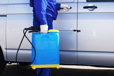 Pest control worker with spray tank near gray minibus outdoors, closeup