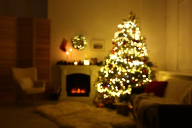 Photo of Blurred view of decorated Christmas tree near fireplace in room. Festive interior design