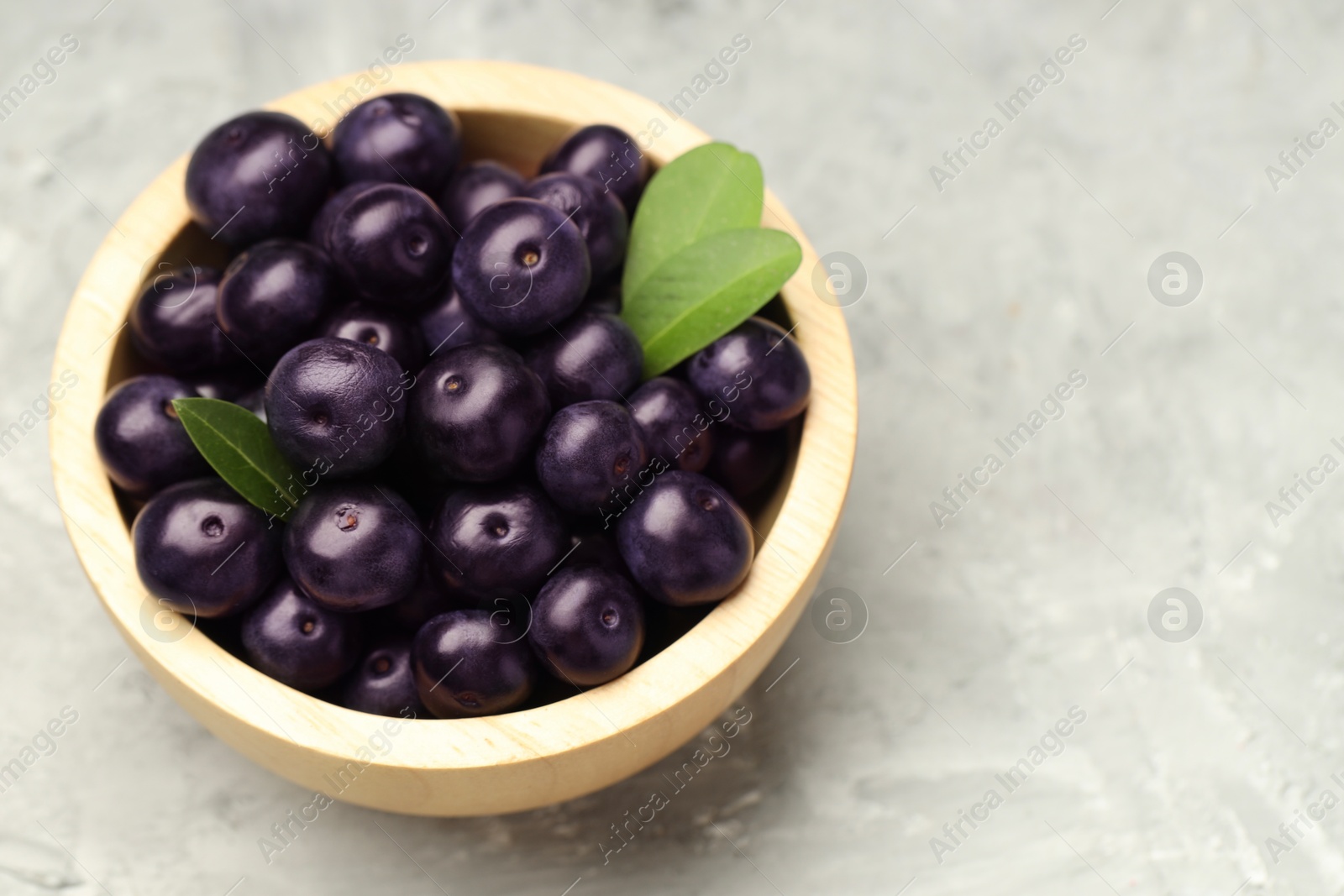 Photo of Ripe acai berries and leaves in bowl on grey textured table, closeup. Space for text