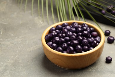 Photo of Ripe acai berries in bowl on grey textured table. Space for text