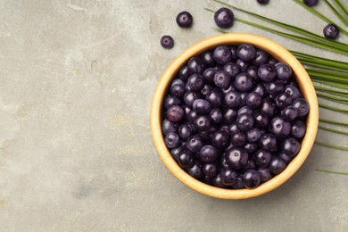 Photo of Ripe acai berries in bowl and palm leaves on grey textured table, flat lay. Space for text