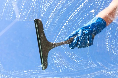 Photo of Woman washing window with squeegee tool against blue sky, closeup