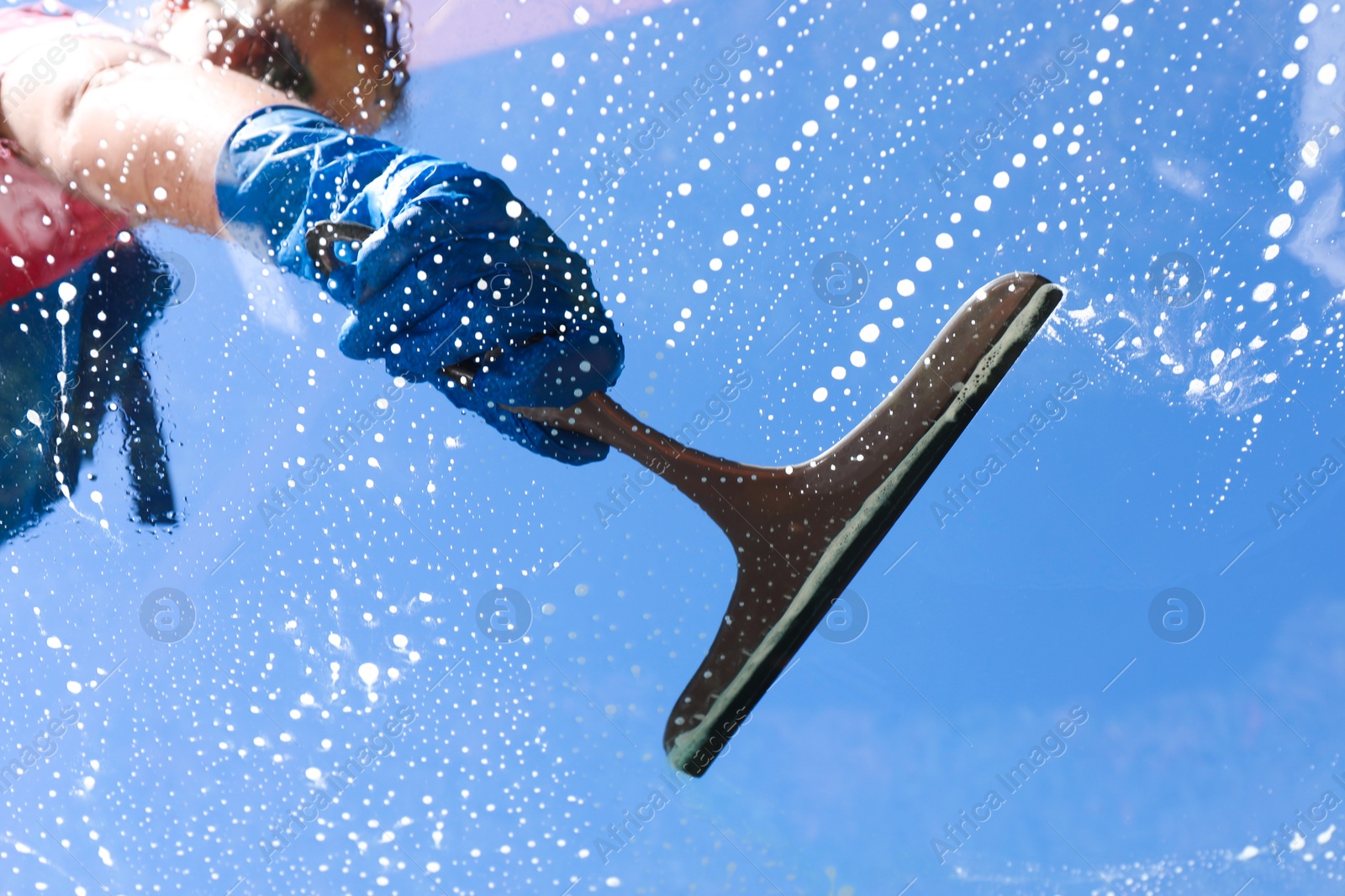 Photo of Woman washing window with squeegee tool against blue sky, closeup