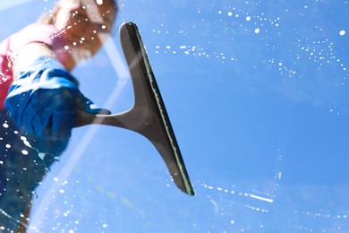 Photo of Woman washing window with squeegee tool against blue sky, closeup