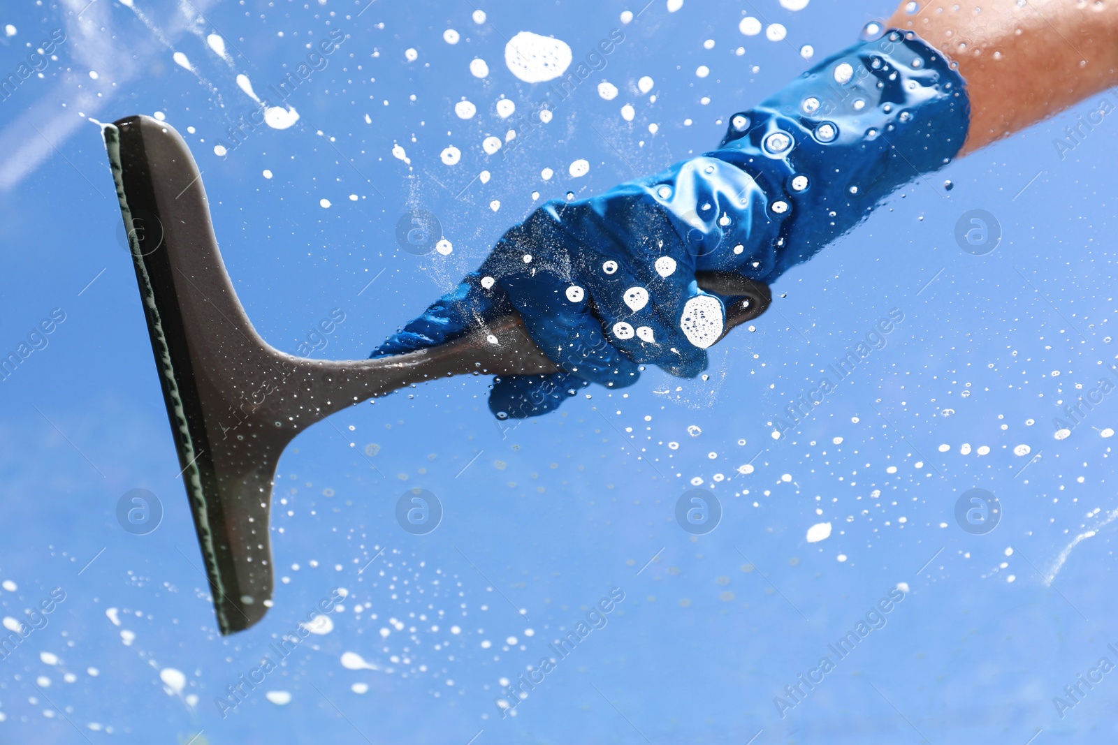 Photo of Woman washing window with squeegee tool against blue sky, closeup