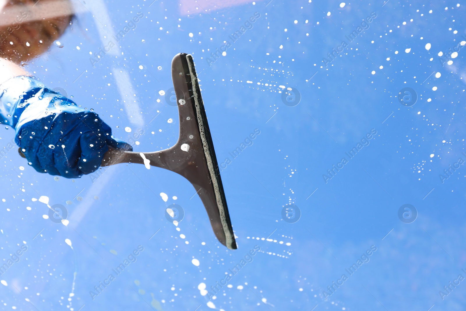 Photo of Woman washing window with squeegee tool against blue sky, closeup