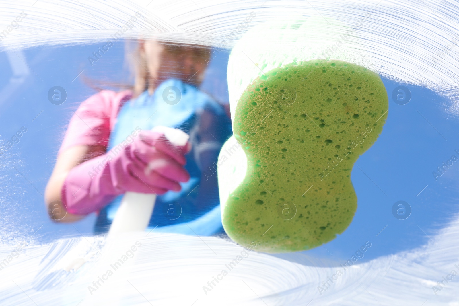 Photo of Woman washing window with sponge against blue sky, closeup