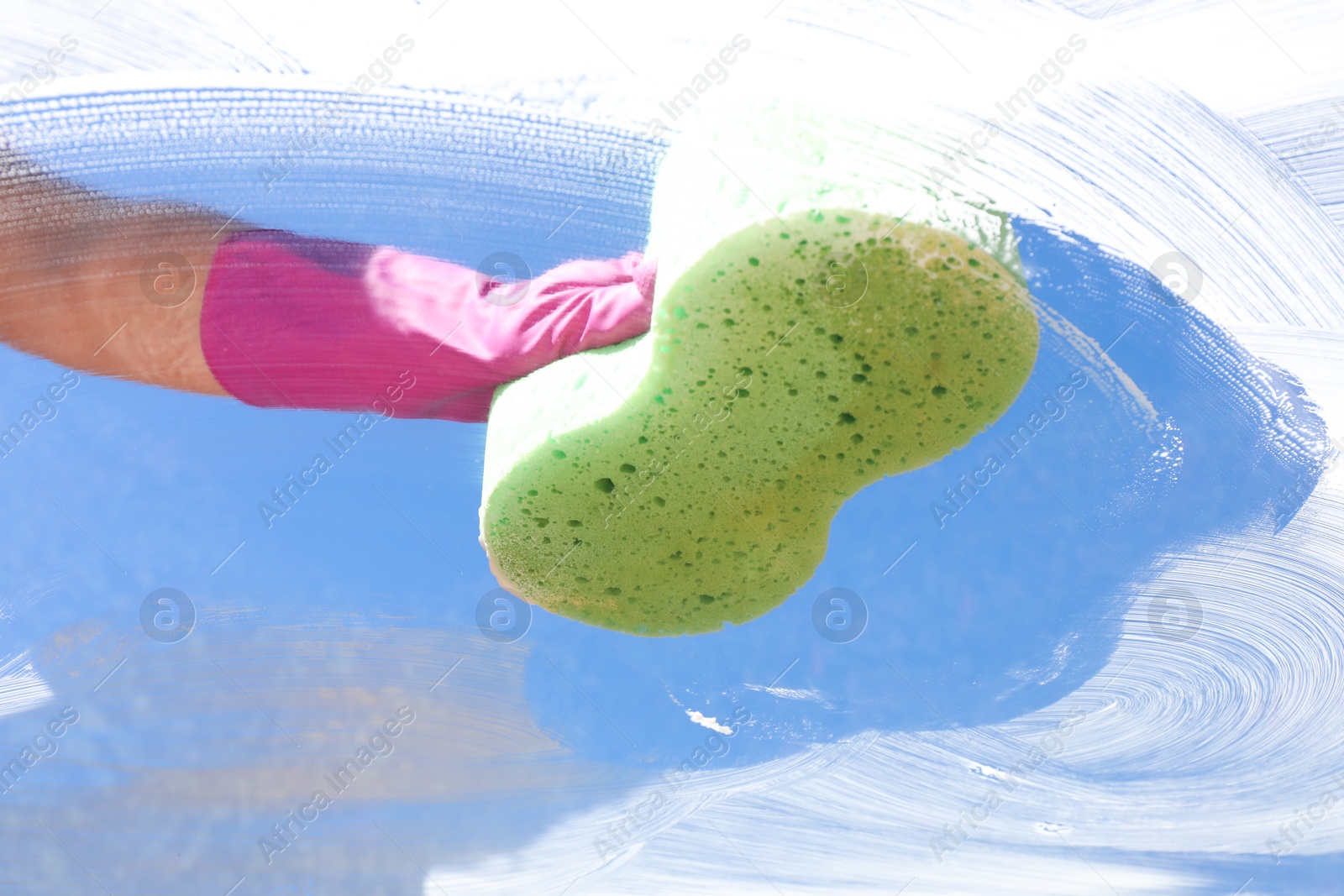 Photo of Woman washing window with sponge against blue sky, closeup