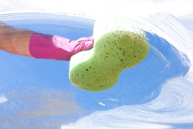 Photo of Woman washing window with sponge against blue sky, closeup