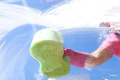 Photo of Woman washing window with sponge against blue sky, closeup