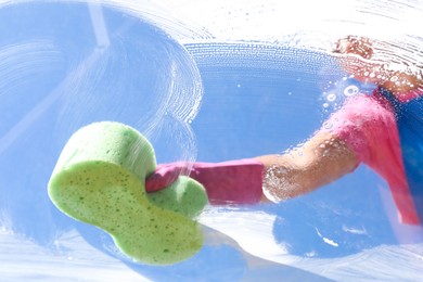 Photo of Woman washing window with sponge against blue sky, closeup