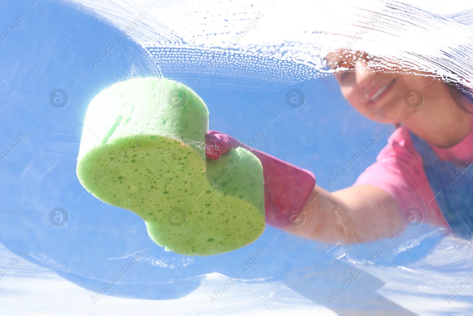 Photo of Woman washing window with sponge against blue sky, closeup