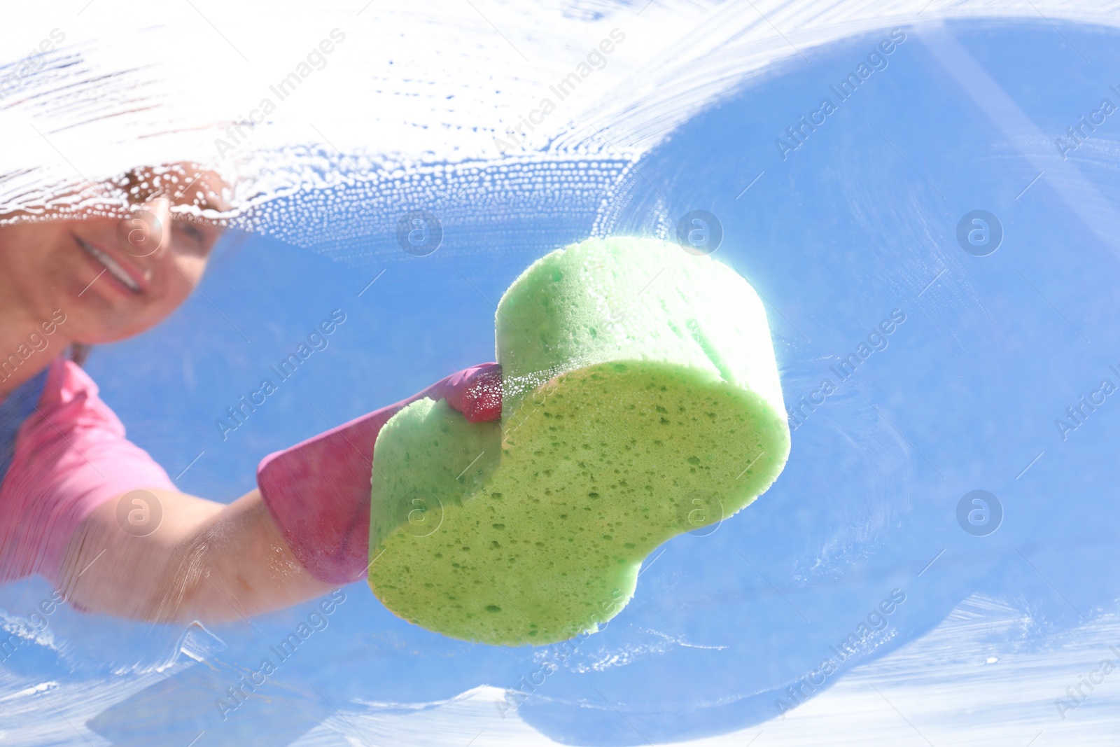 Photo of Woman washing window with sponge against blue sky, closeup