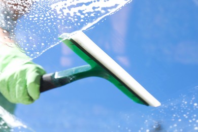 Photo of Woman washing window with squeegee tool against blue sky, closeup