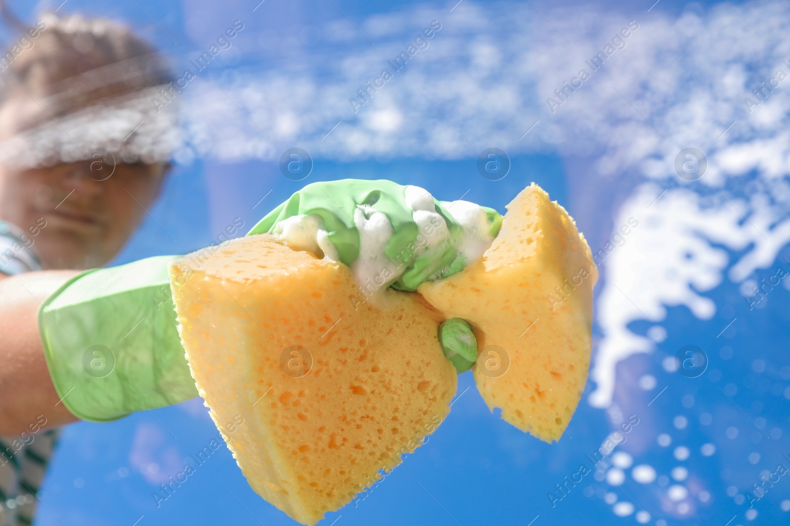 Photo of Woman washing window with sponge against blue sky, closeup