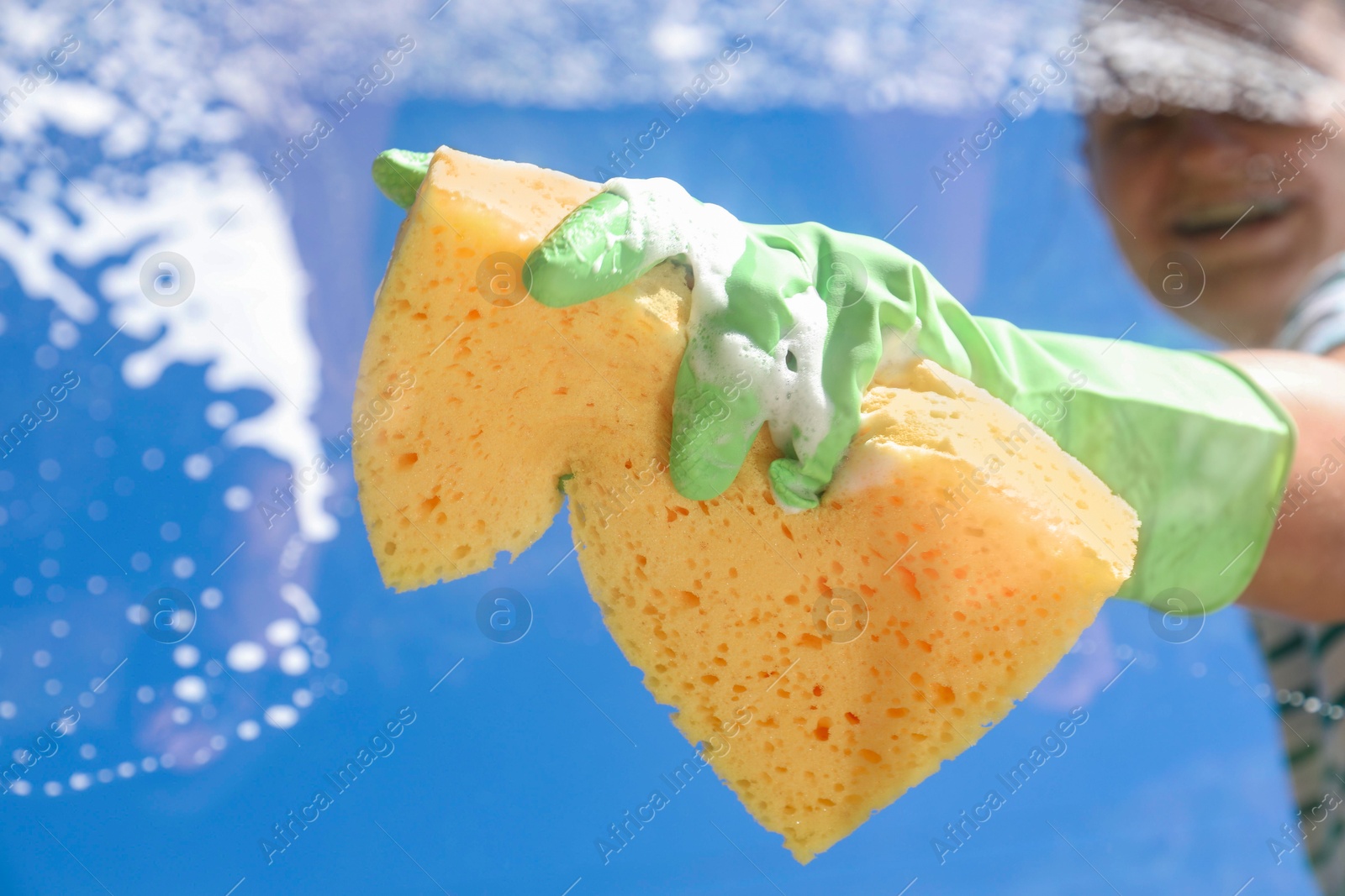 Photo of Woman washing window with sponge against blue sky, closeup