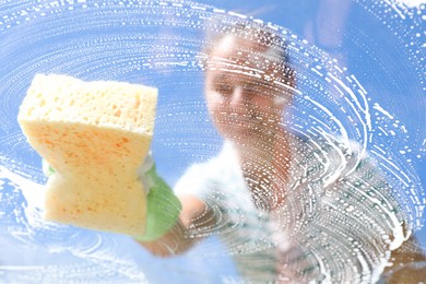 Photo of Woman washing window with sponge against blue sky, closeup