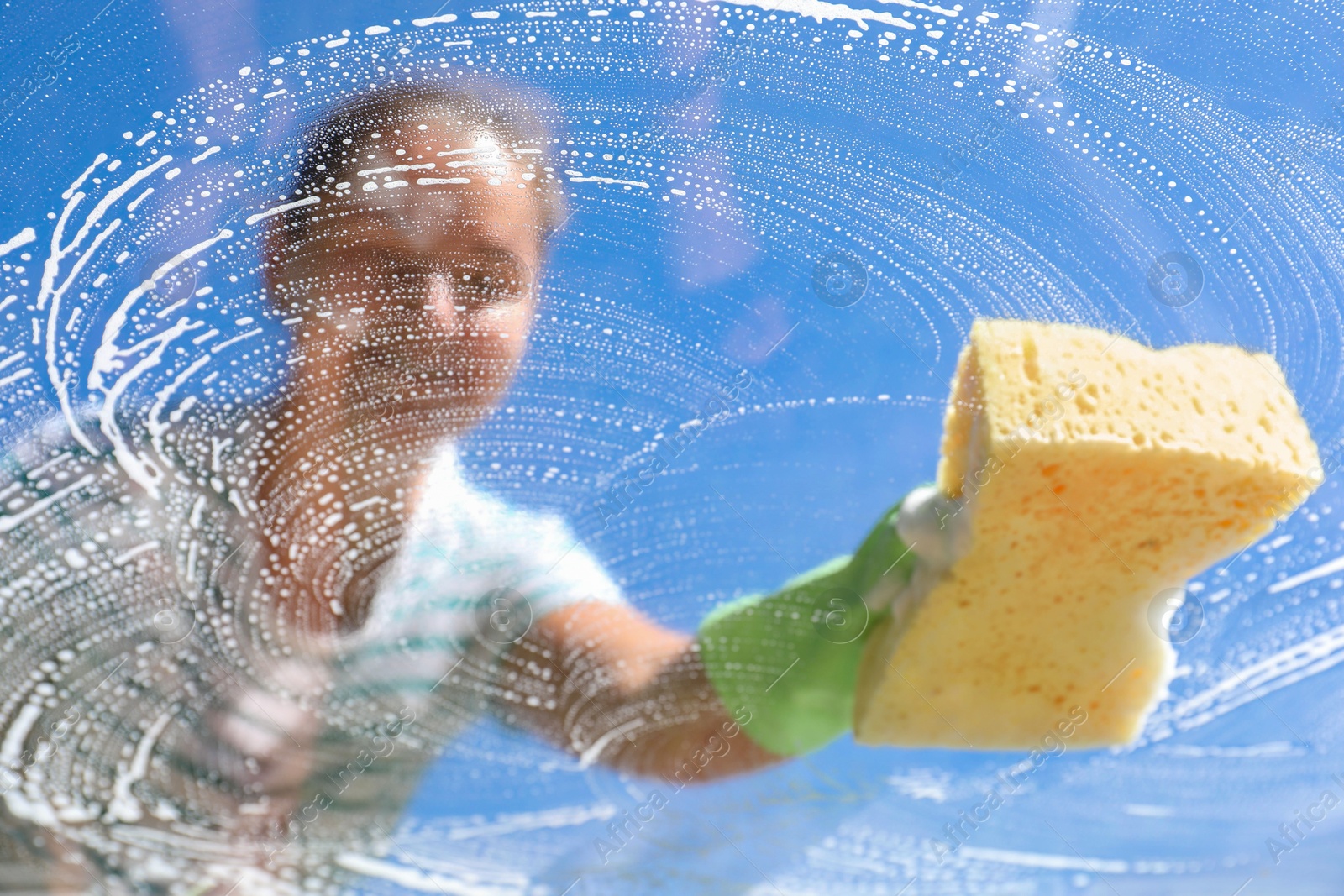 Photo of Woman washing window with sponge against blue sky, closeup