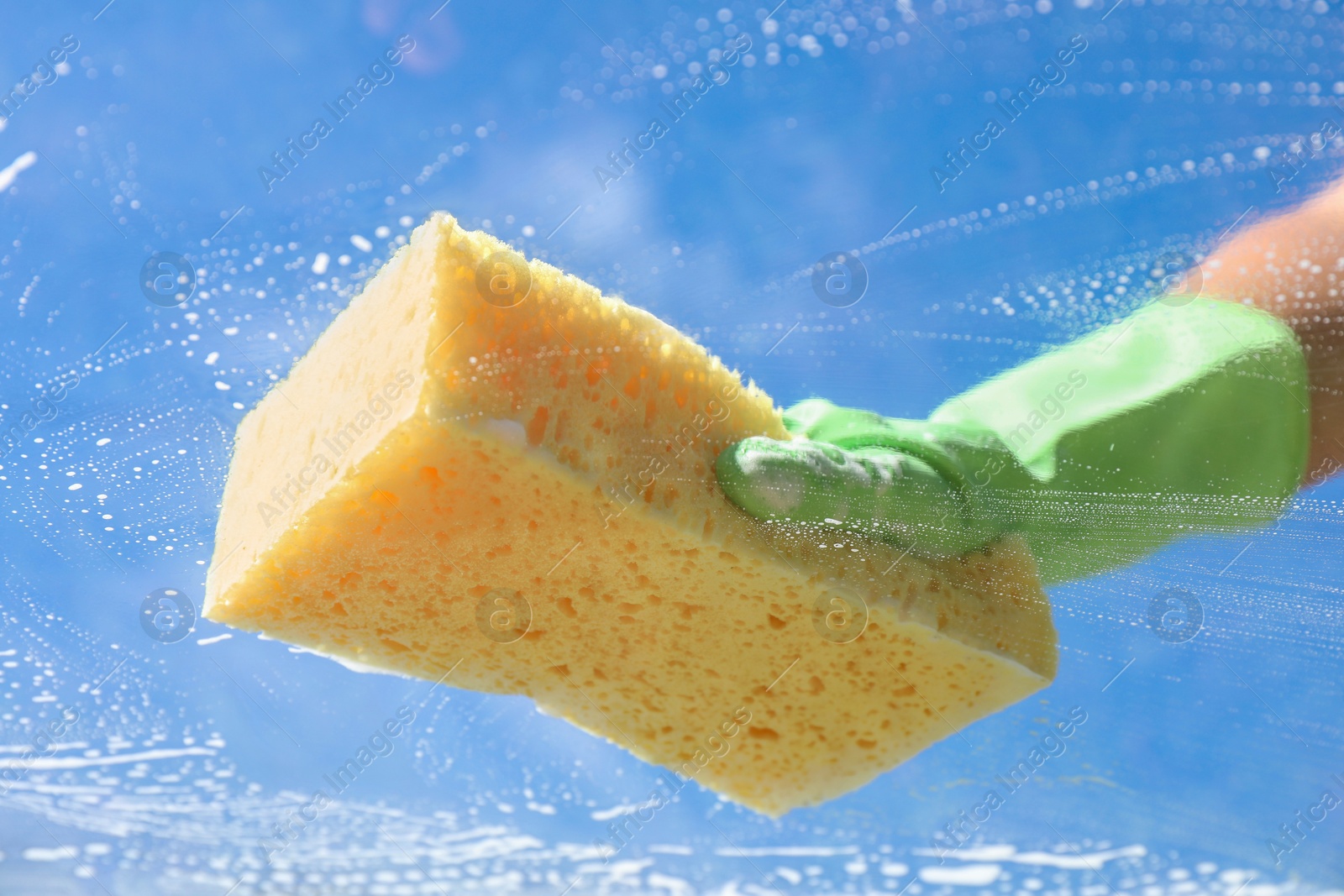 Photo of Woman washing window with sponge against blue sky, closeup