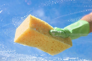 Photo of Woman washing window with sponge against blue sky, closeup