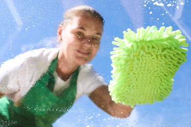 Photo of Woman washing window with microfiber mitt against blue sky, closeup