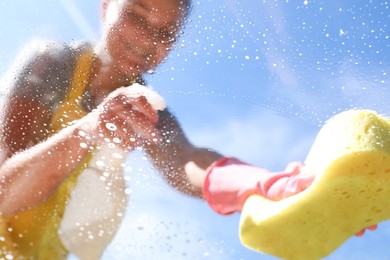 Photo of Woman washing window with sponge against blue sky, closeup