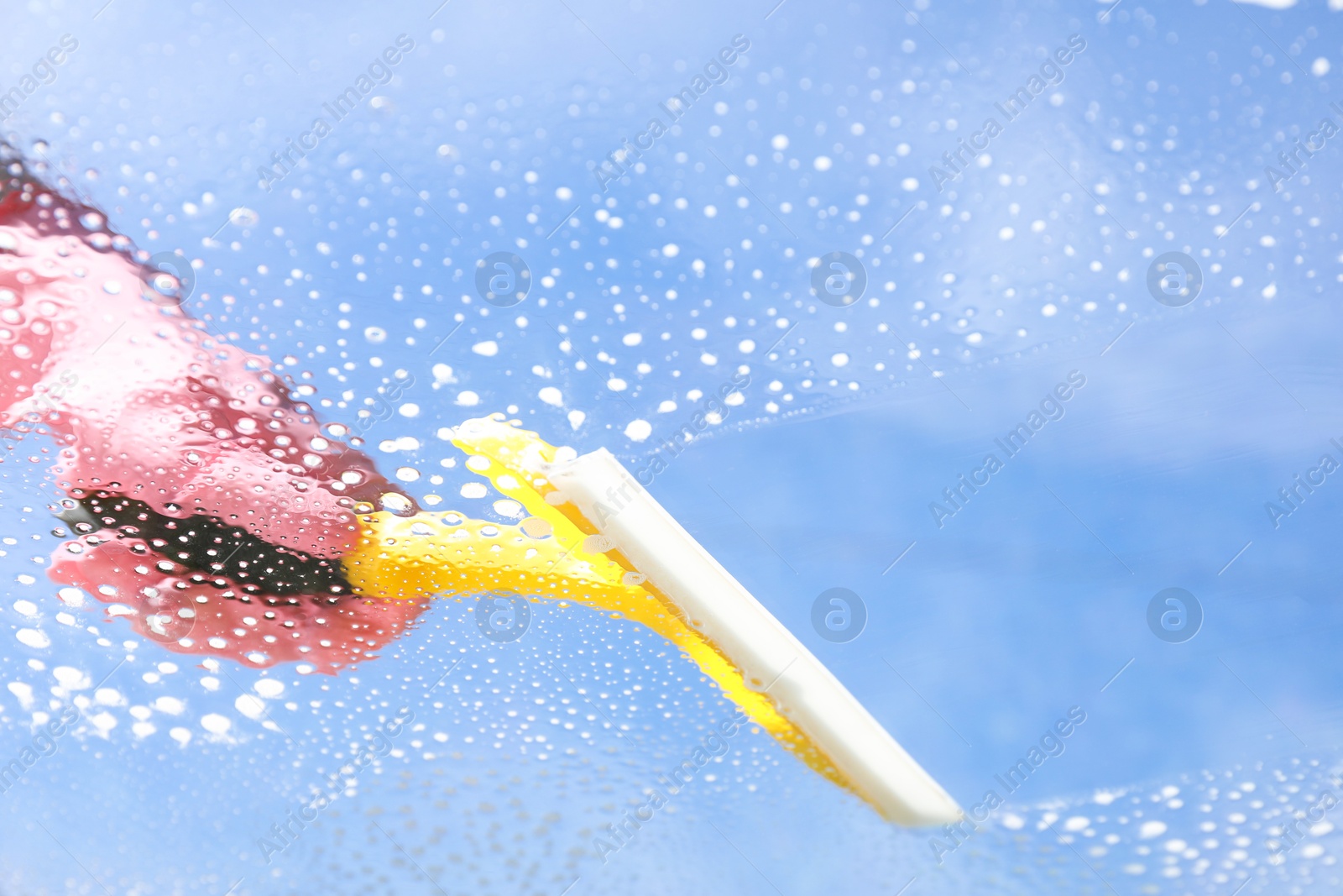 Photo of Woman washing window with squeegee tool against blue sky, closeup