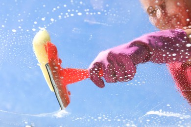 Photo of Woman washing window with squeegee tool against blue sky, closeup