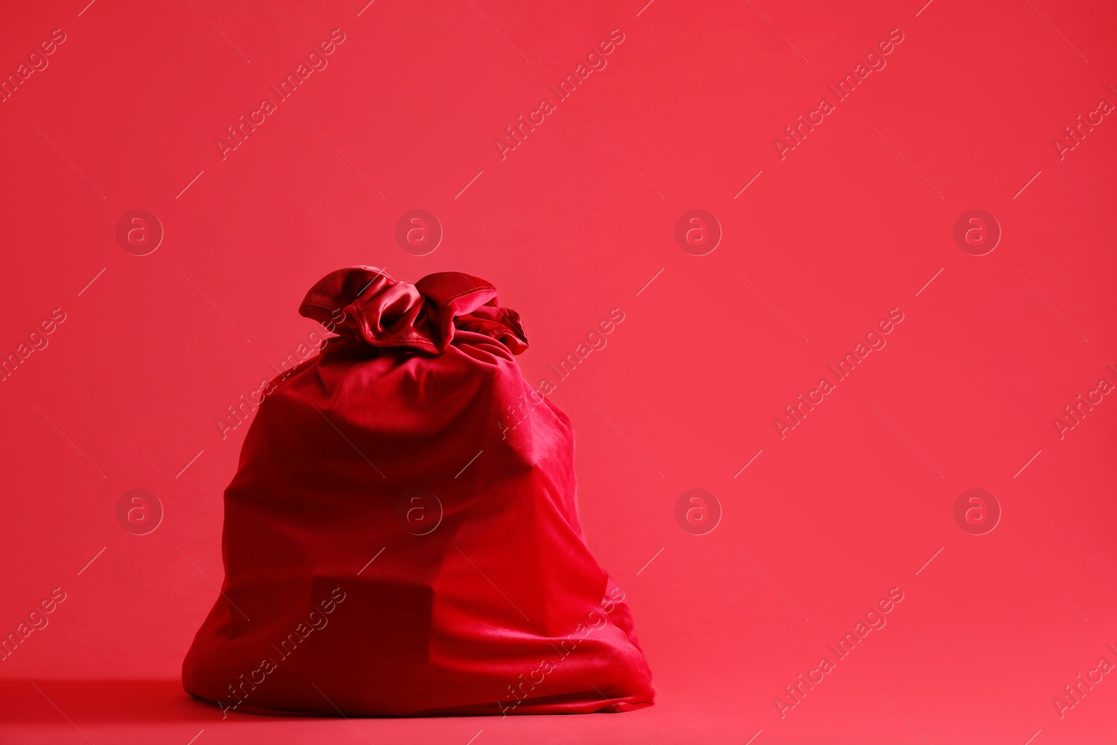 One Santa Claus bag on red background, space for text Photo of One Santa Claus bag on red background, space for text