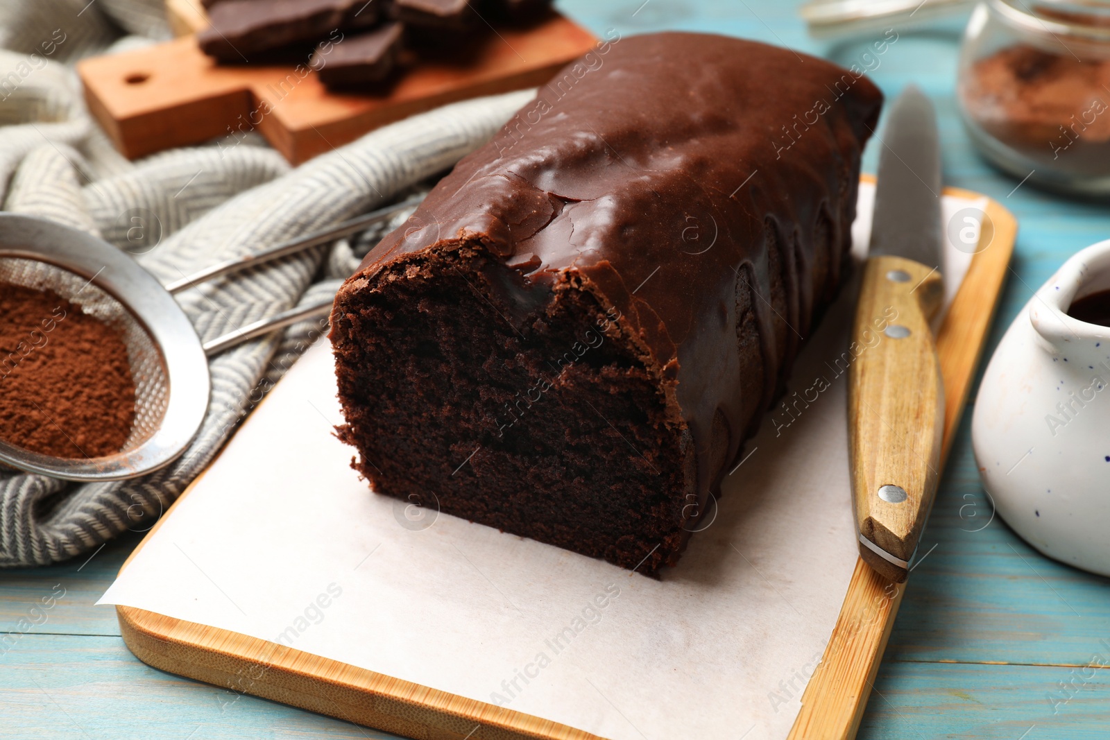 Photo of Tasty chocolate sponge cake and cocoa powder on light blue wooden table, closeup