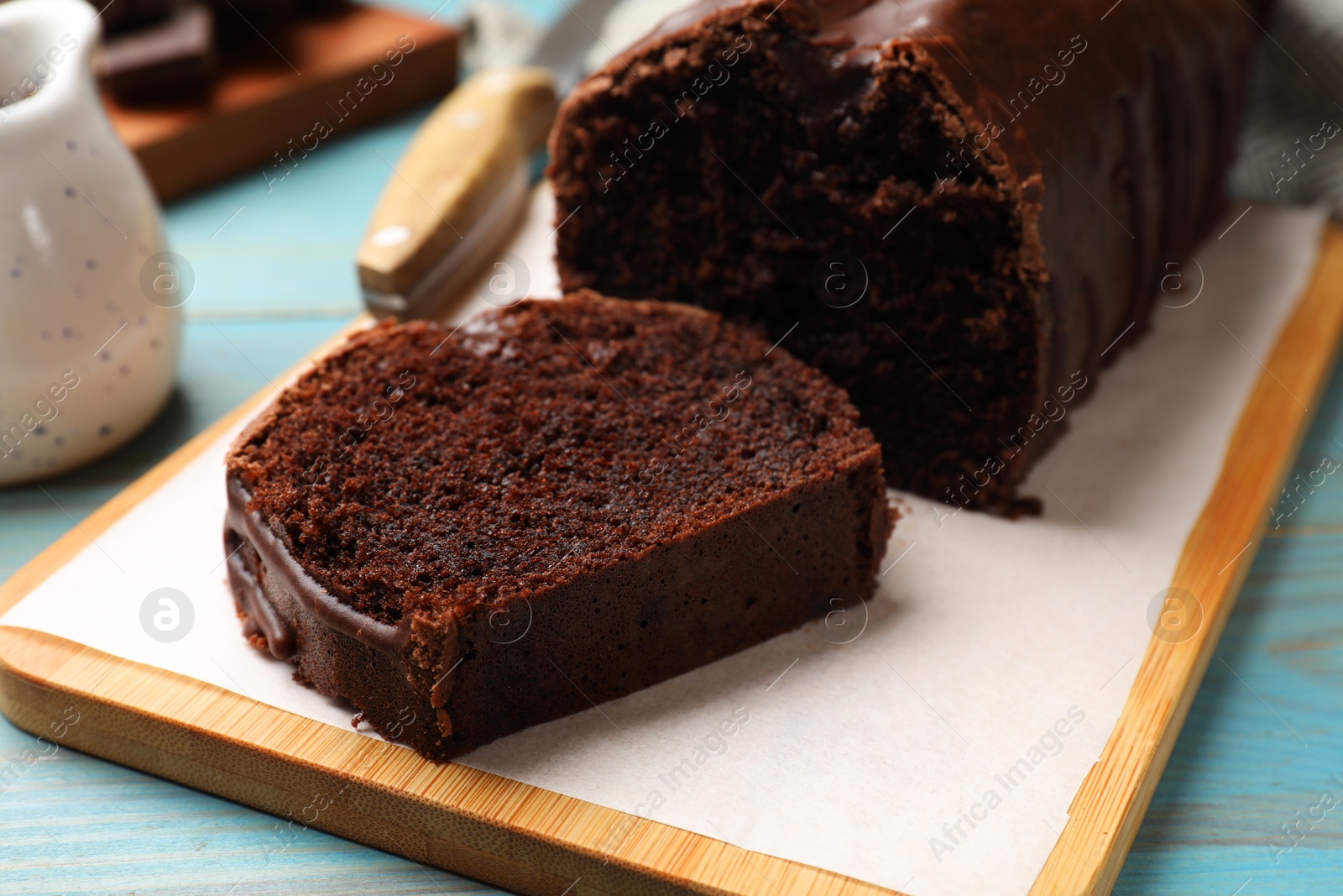 Photo of Tasty chocolate sponge cake on light blue wooden table, closeup