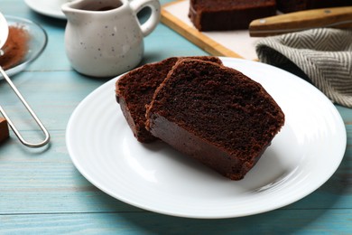 Photo of Slices of tasty chocolate sponge cake on light blue wooden table, closeup